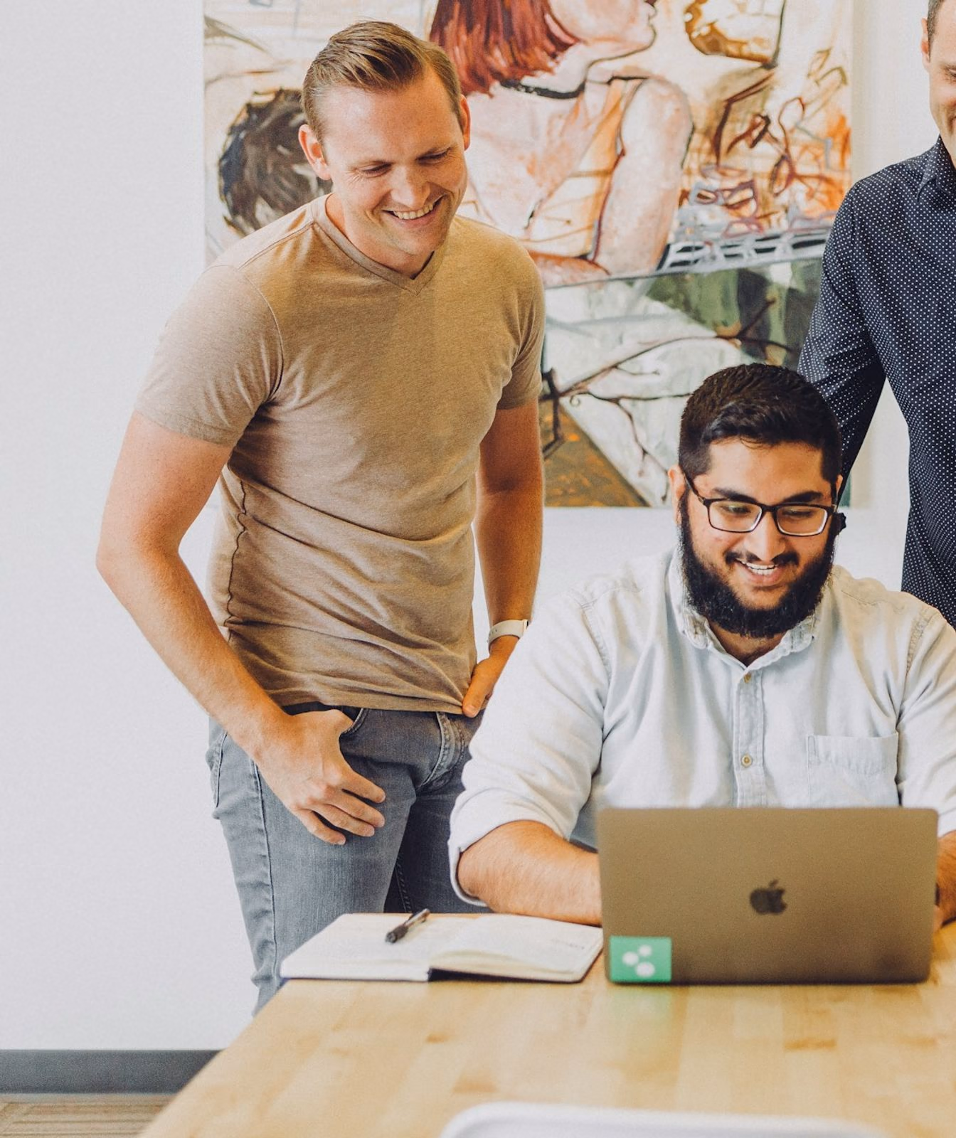 Four colleagues gathered around a laptop at a shared table.