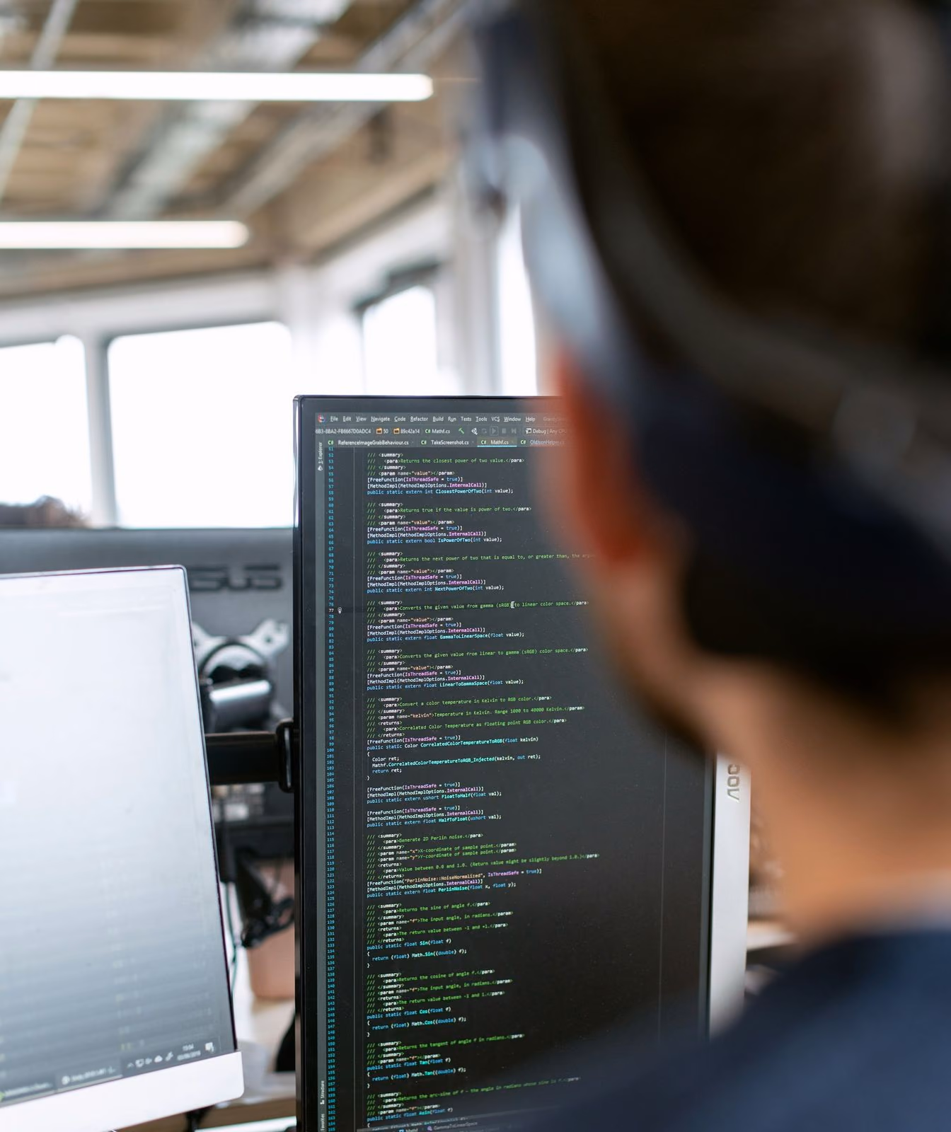 Engineer reading code on a large monitor in a dimly lit workspace.